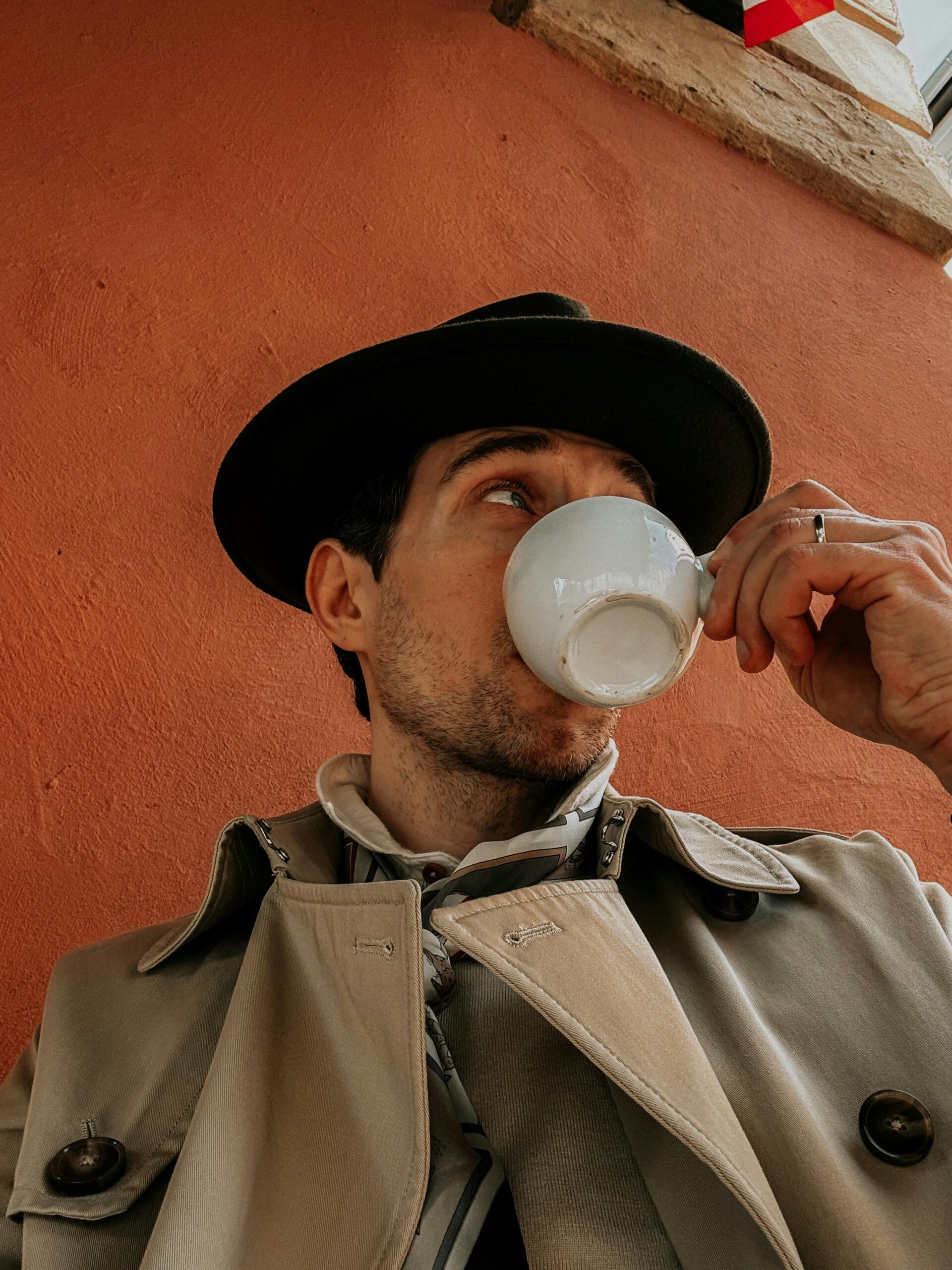 A fashionable man enjoys coffee against a textured orange wall in Lower Silesian Voivodeship.